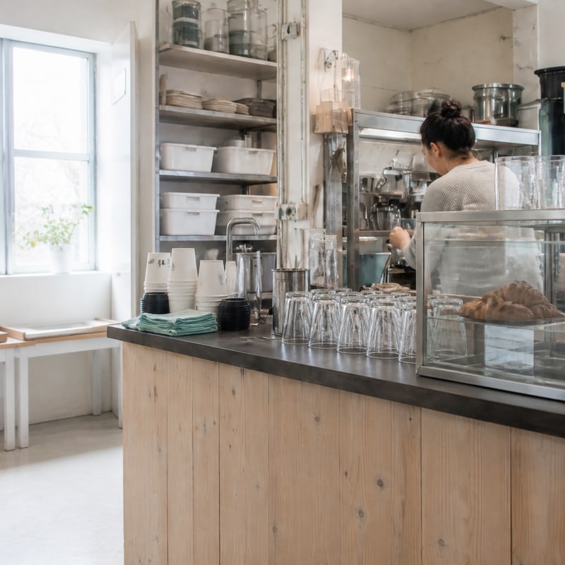 A cafe bar counter mid-service, glassware and bottles on the back wall.